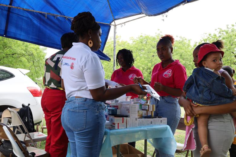 A mother holds her child in her left arm while receiving medication after a consultation for the child’s flu at the mobile clinic organized by the Haitian Midwives Association (ASFH) at the Quiskeya Chapel in Delmas 75, on Saturday, May 3, 2025. Photo by Dieugo André for The Haitian Times.
