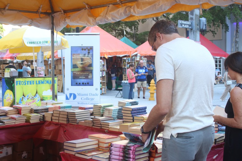 A visitor examines books on display at a vendor tent during the Street Fair at the Miami Book Fair on Sunday, Nov. 23, 2025. Photo by Béatrice Vallières for The Haitian Times.