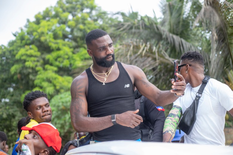 Frantzdy Pierrot takes selfies with fans as he arrives in Bas-Limbé on Friday, July 10, 2026, riding on the back of a pickup truck. Photo by Ketlain Difficile for The Haitian Times.